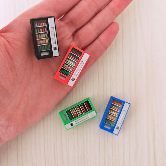 Three miniature 1:64 vending machines (black, red, blue and green) held in a person’s hand to show size reference.