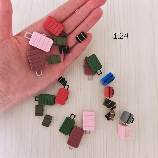 Miniature 3D-printed suitcases in scale 1:24, held in a person’s hand for size reference. Includes various colors such as red, pink, green, and brown.