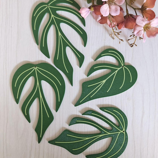 Four Monstera Burle Marx Flame leaf coasters arranged flat on a light wood surface.