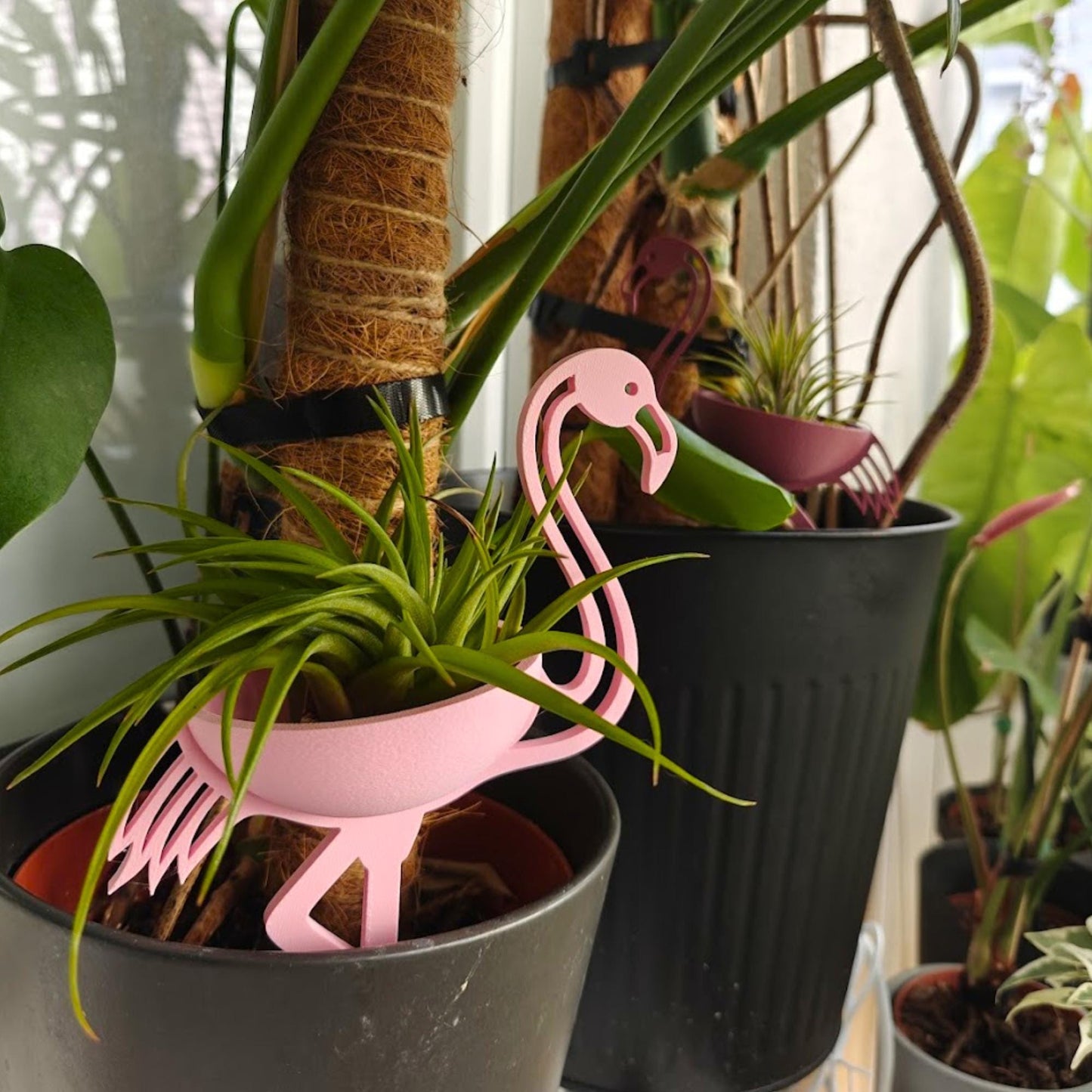 Pink flamingo plant holder placed inside pot among houseplants