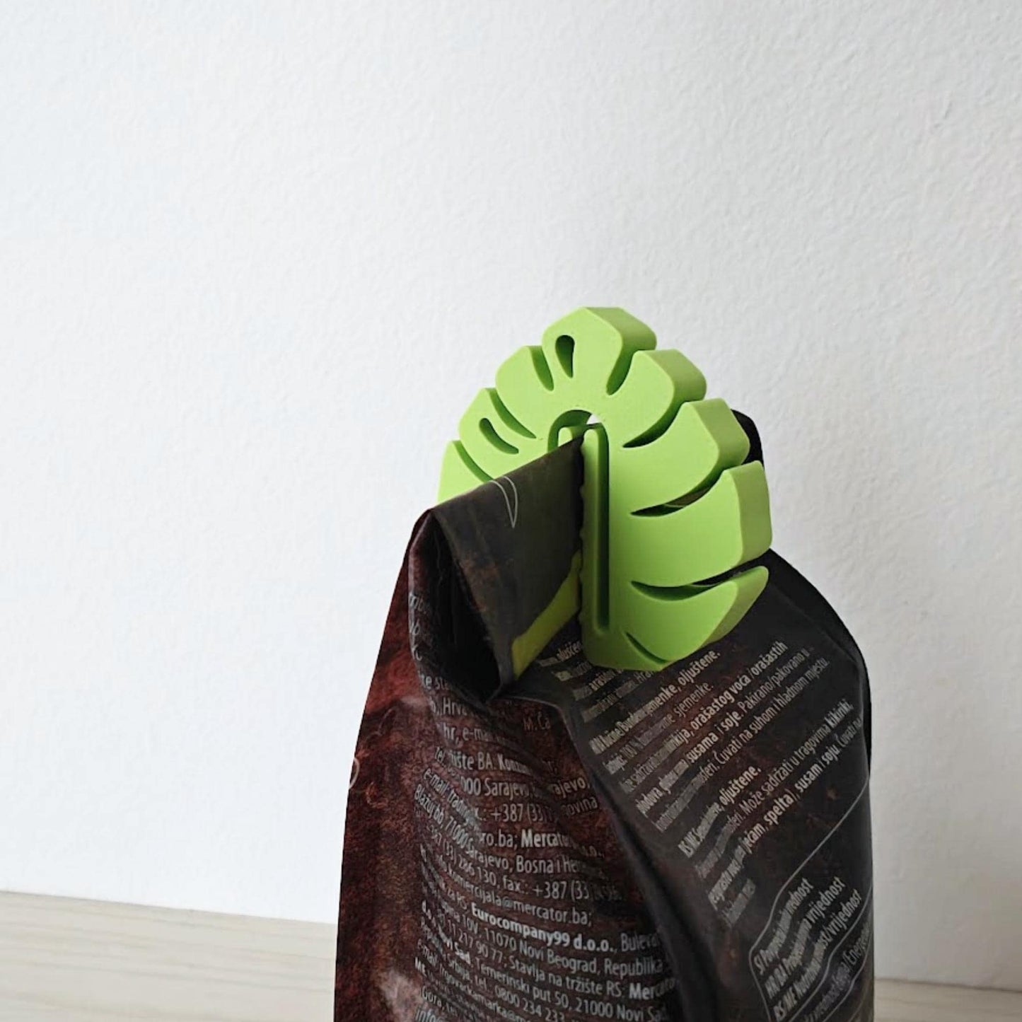 Bright green leaf-shaped clip closing a dark paper bag, shown close up.