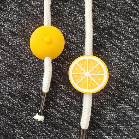 Yellow citrus drawstring charm on white cords, shown on dark gray sweatshirt fabric.