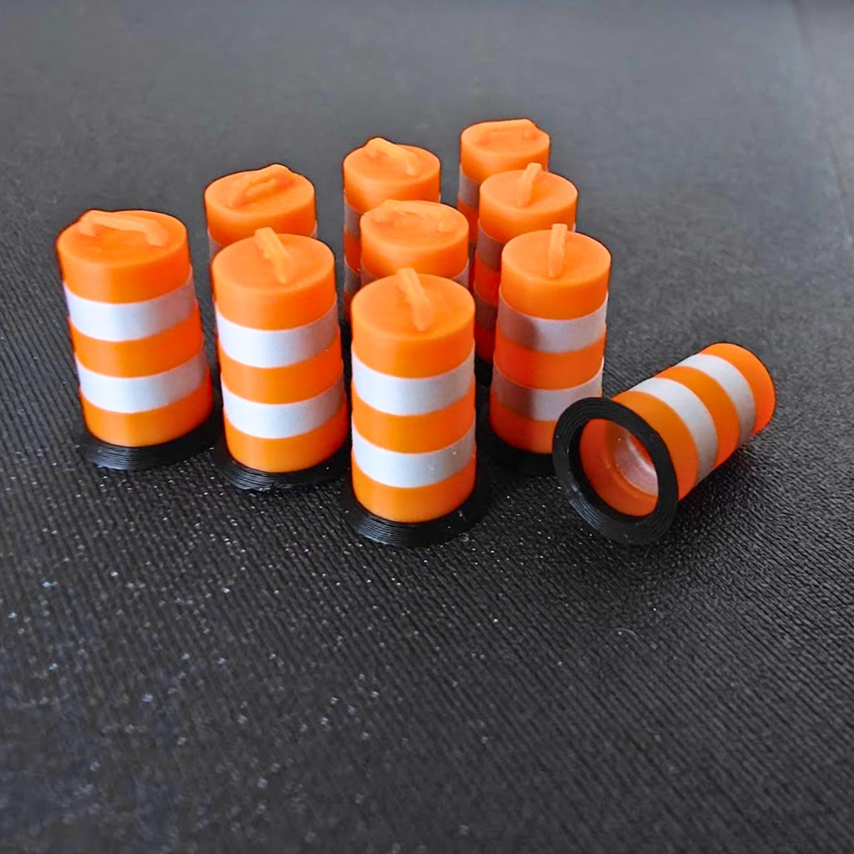 Close-up of miniature orange traffic barrels with metallic silver bands, including one barrel lying on its side.