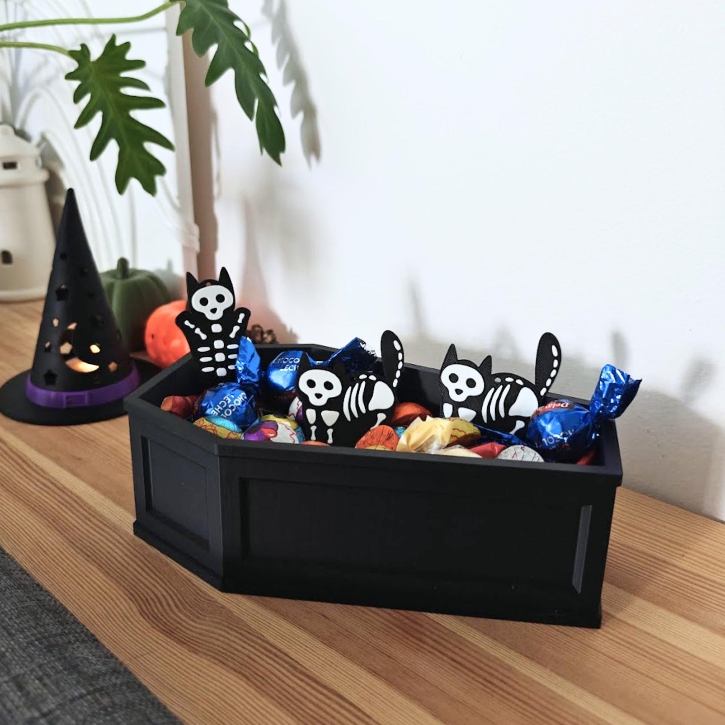 Coffin candy bowl displayed on a shelf with candies and skeleton decorations in a cozy Halloween setup.