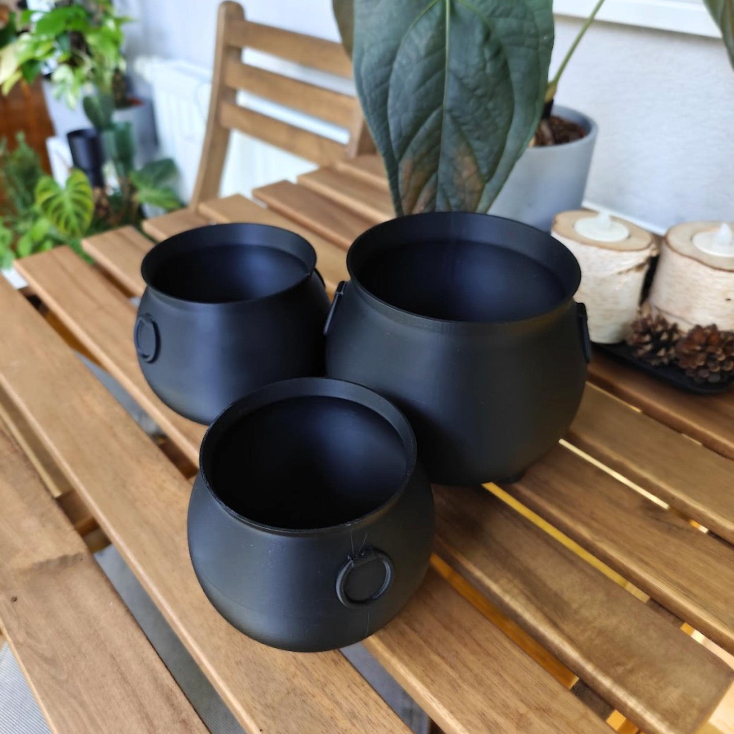 Set of three black cauldron planters placed together on a wooden tabletop.
