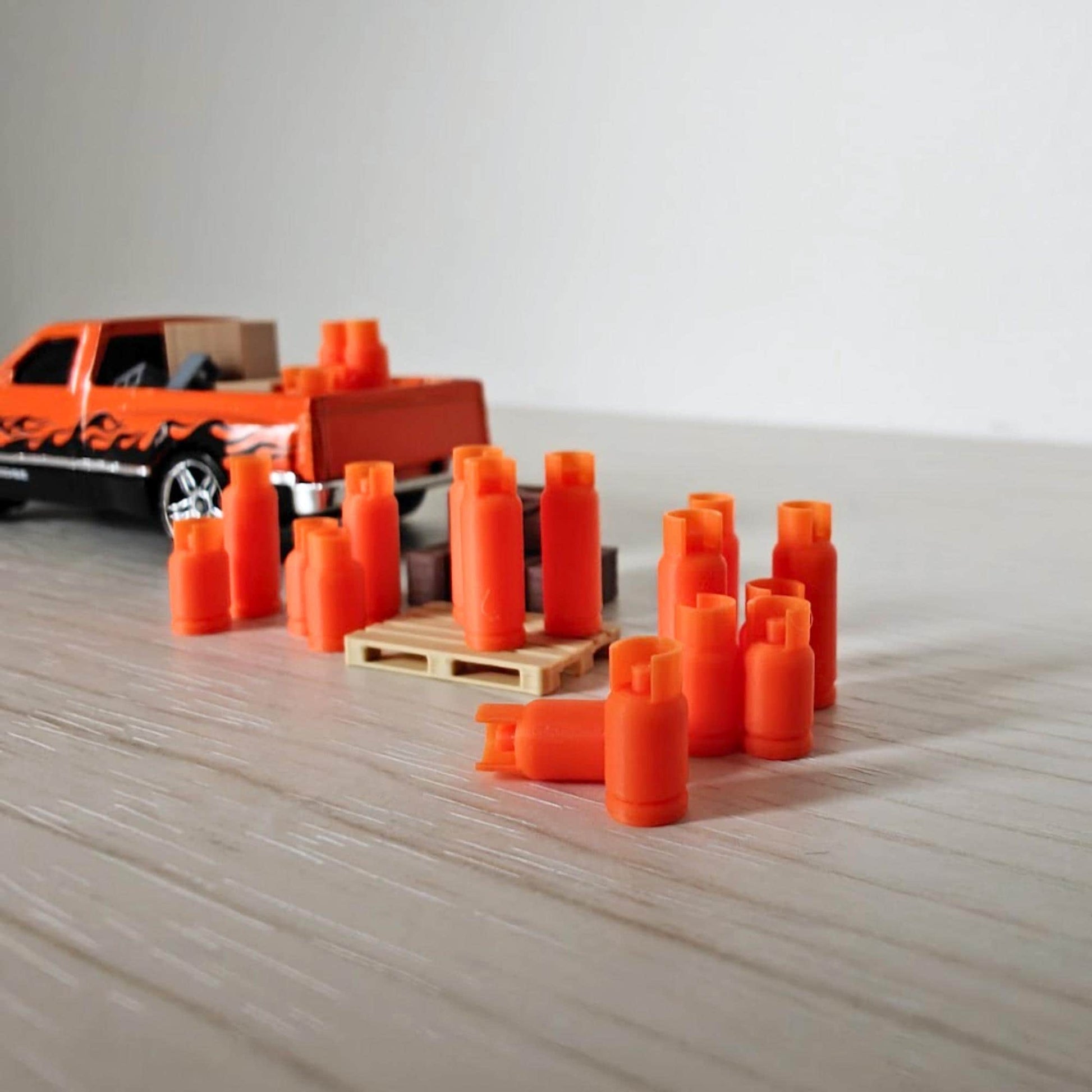Miniature orange gas bottles arranged beside a 1:64 scale pickup truck, displayed on a light wooden surface.