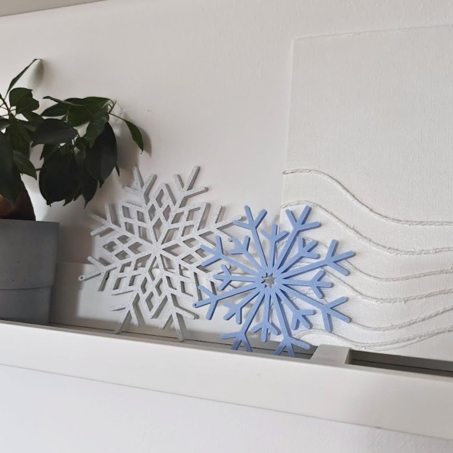 Large 3D-printed snowflake decorations in marble and blue arranged on a shelf with holiday decor.