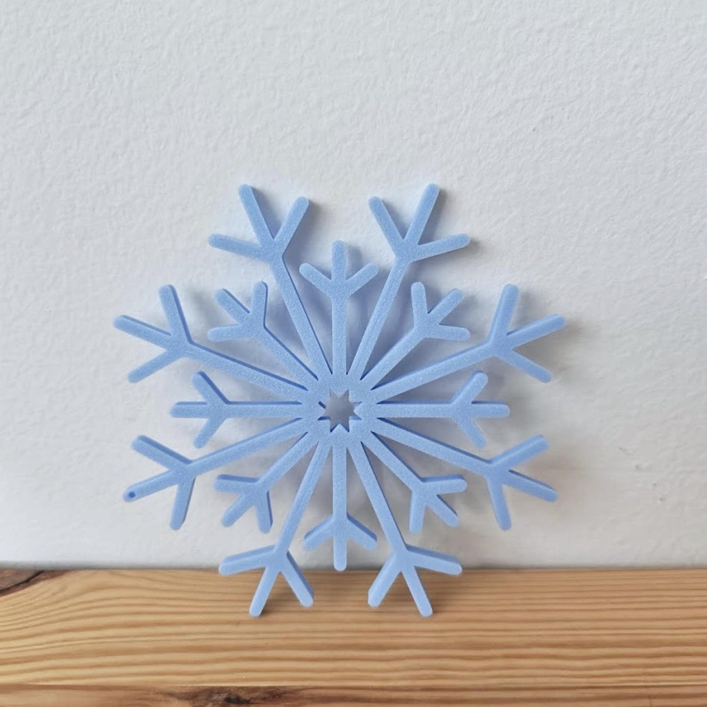 Close-up of a blue 3D-printed snowflake ornament placed on a wooden surface.
