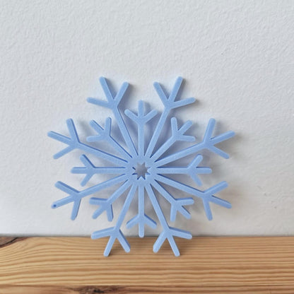Close-up of a blue 3D-printed snowflake ornament placed on a wooden surface.