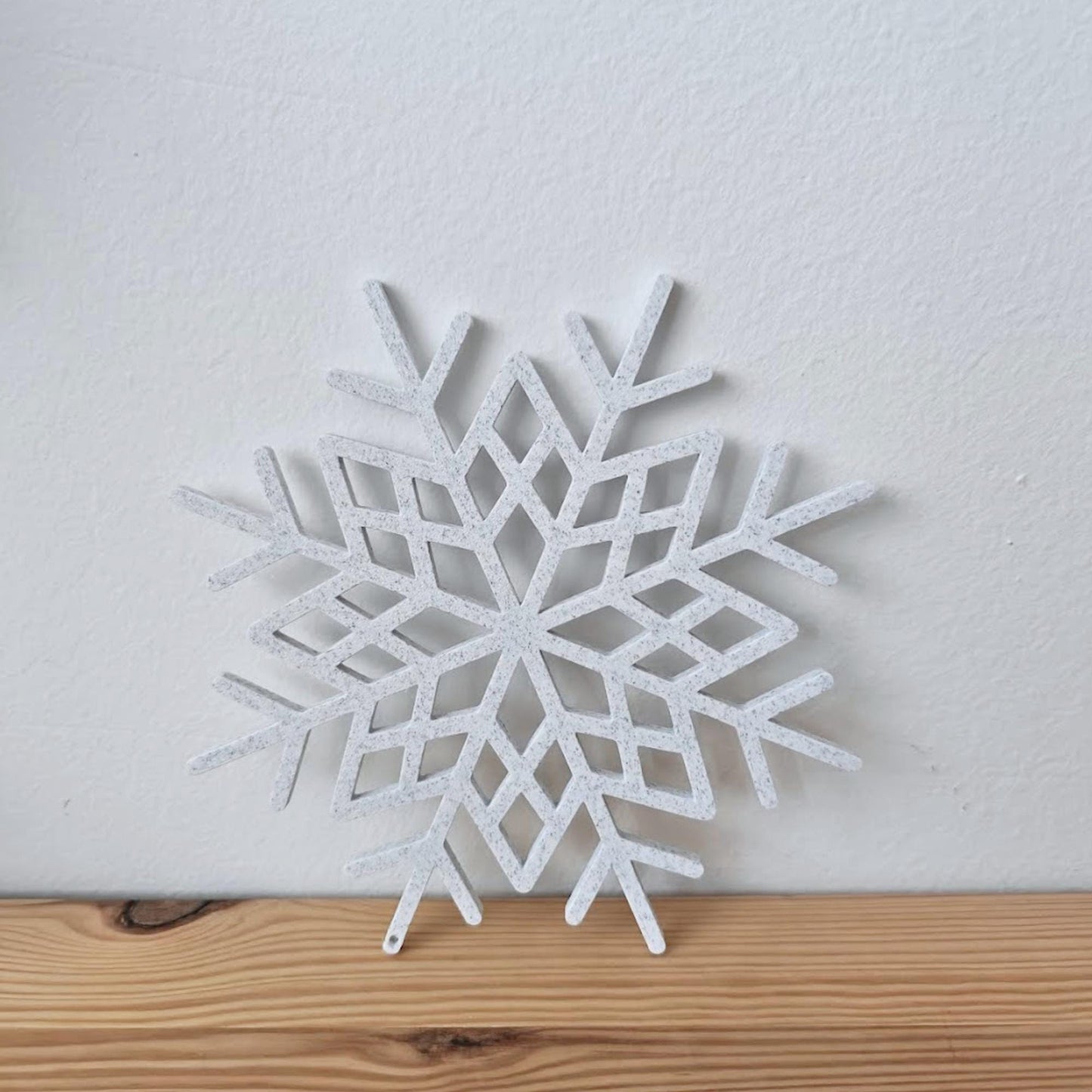 Close-up of a marble 3D-printed snowflake ornament placed on a wooden surface.