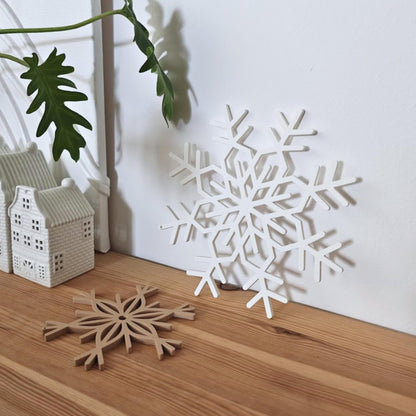 Latte brown and white snowflake decorations on a wooden surface beside a holiday candle holder.