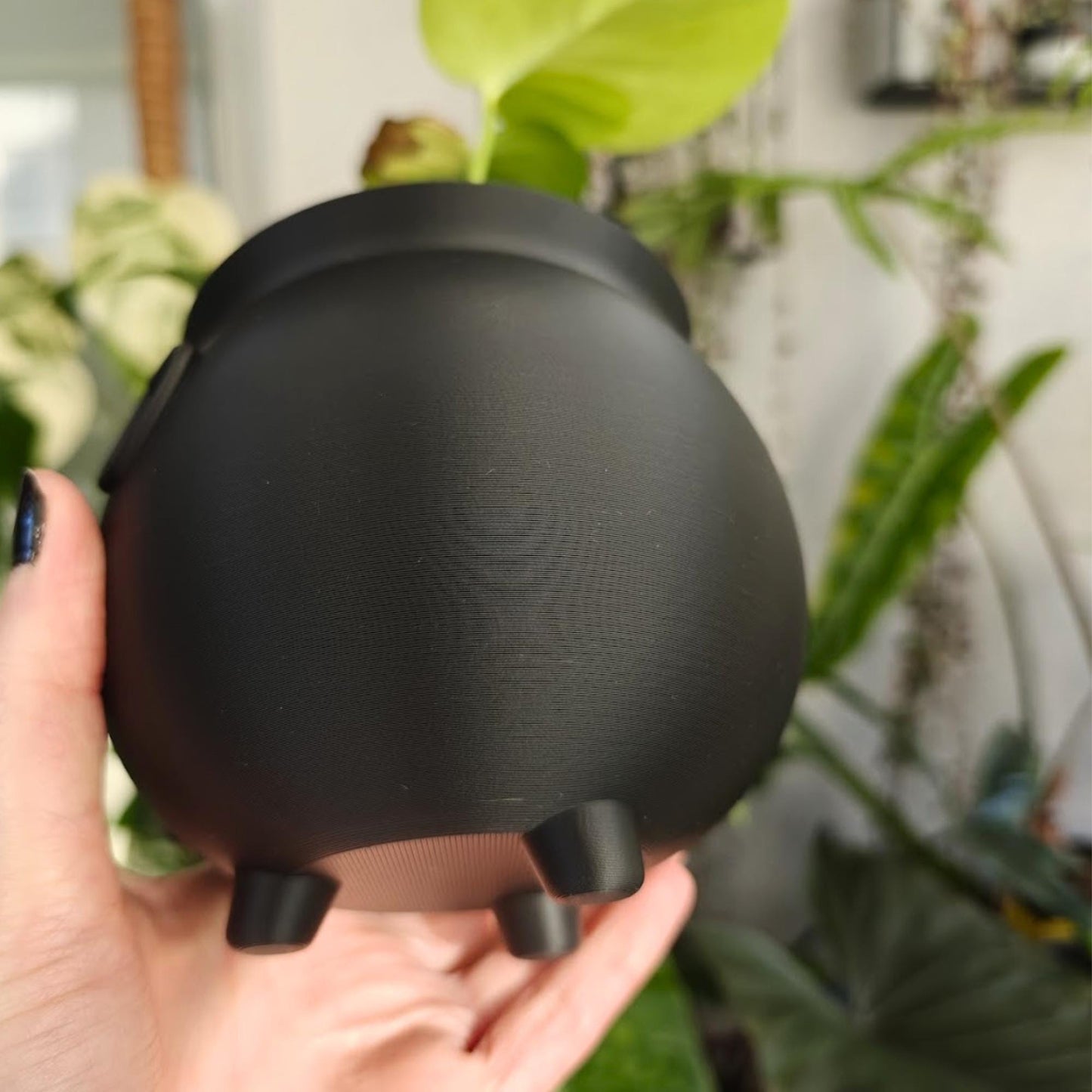 Bottom view of a 3D-printed cauldron planter showing smooth rounded base and three small legs.