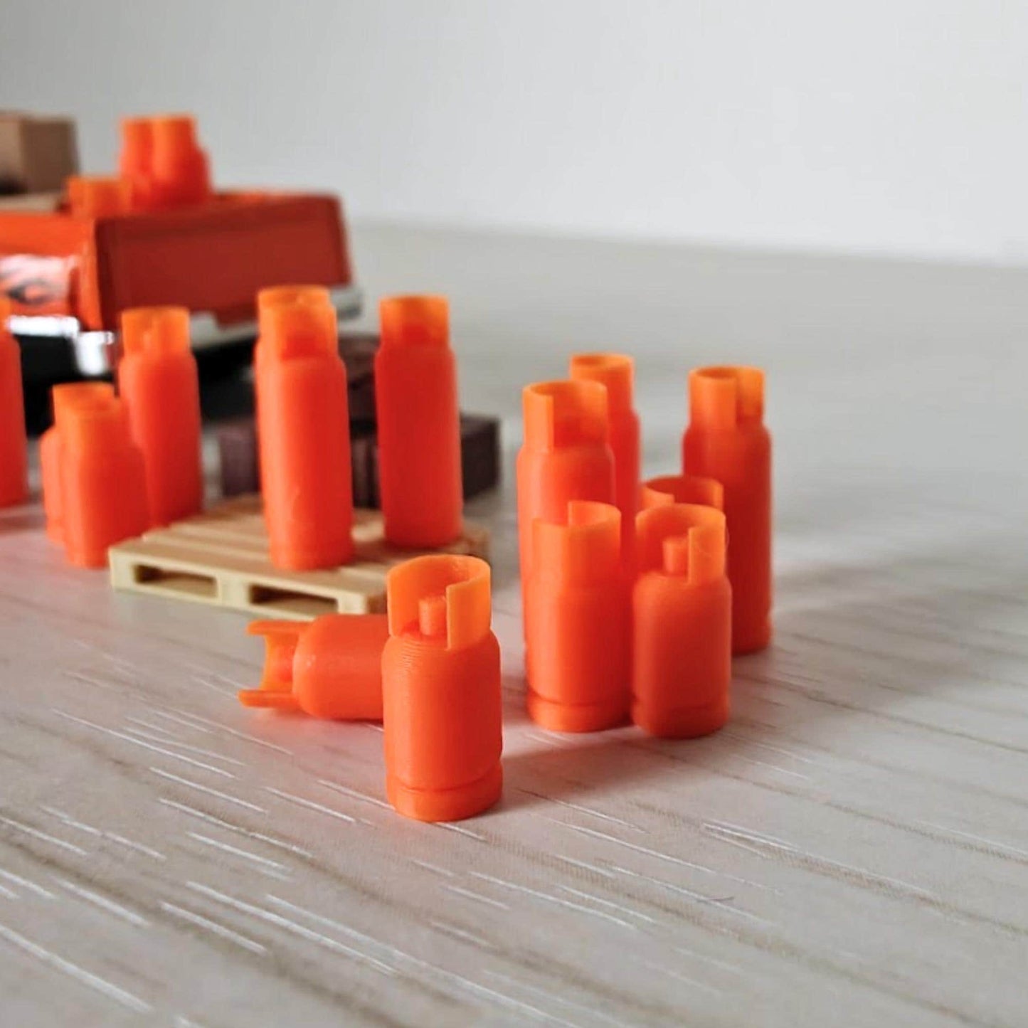 Collection of tiny orange gas bottles arranged in rows near a model truck and pallet, showing diorama setup.