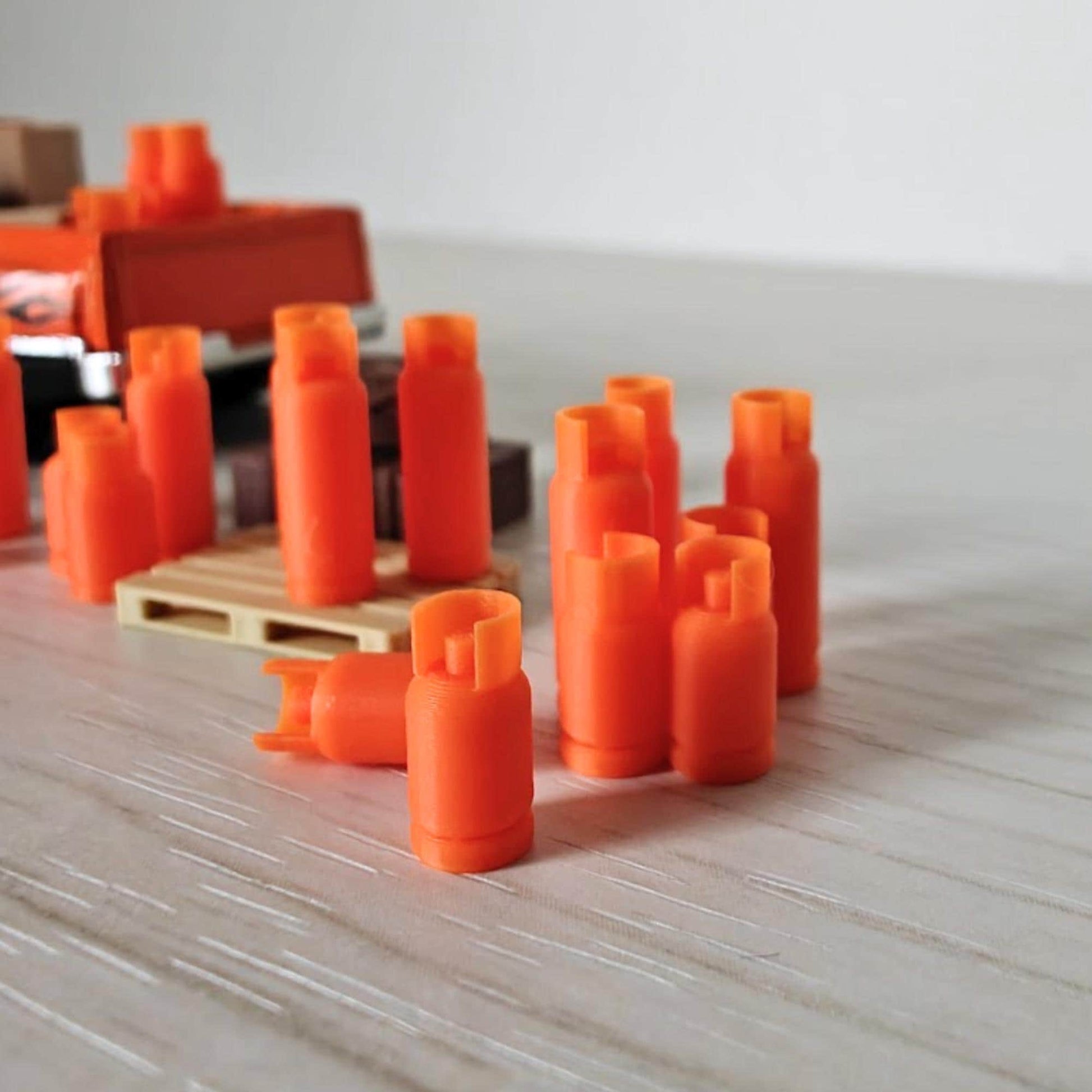 Collection of tiny orange gas bottles arranged in rows near a model truck and pallet, showing diorama setup.