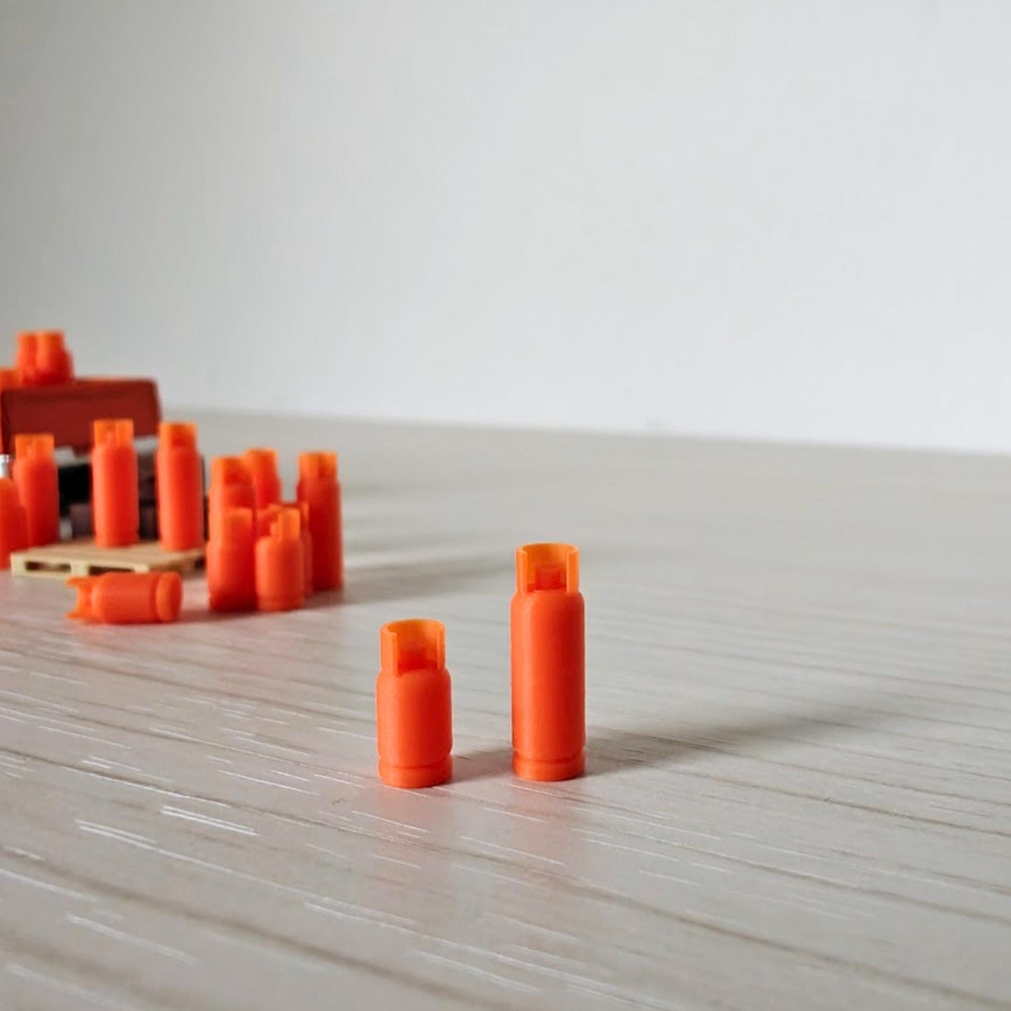 Close-up of small and large orange 1:64 scale gas bottles standing side by side on a wooden surface.