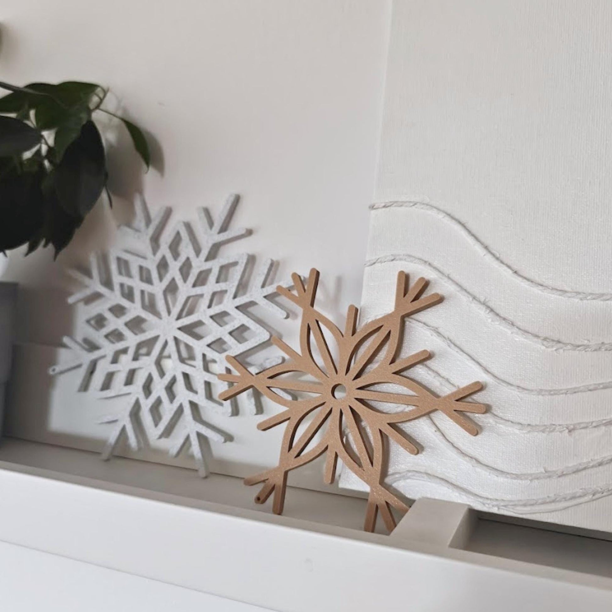 Large 3D-printed snowflake decorations in white and latte brown arranged on a shelf with holiday decor.