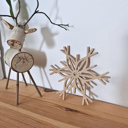 LLatte brown snowflake ornament leaning against a wall, next to Christmas decor.