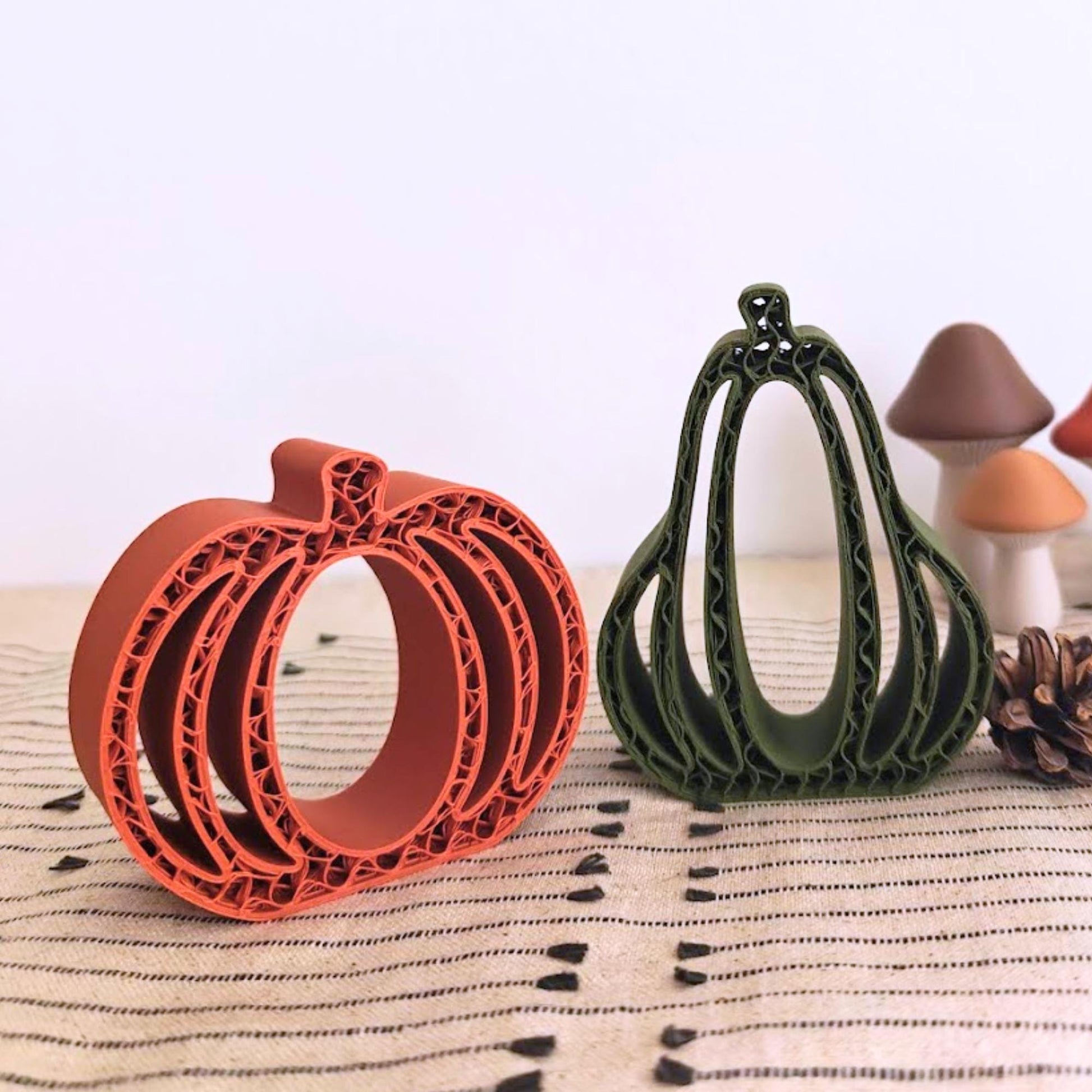 Close-up of orange and green 3D-printed pumpkins and gourds with small decorative leaves on a beige woven cloth.