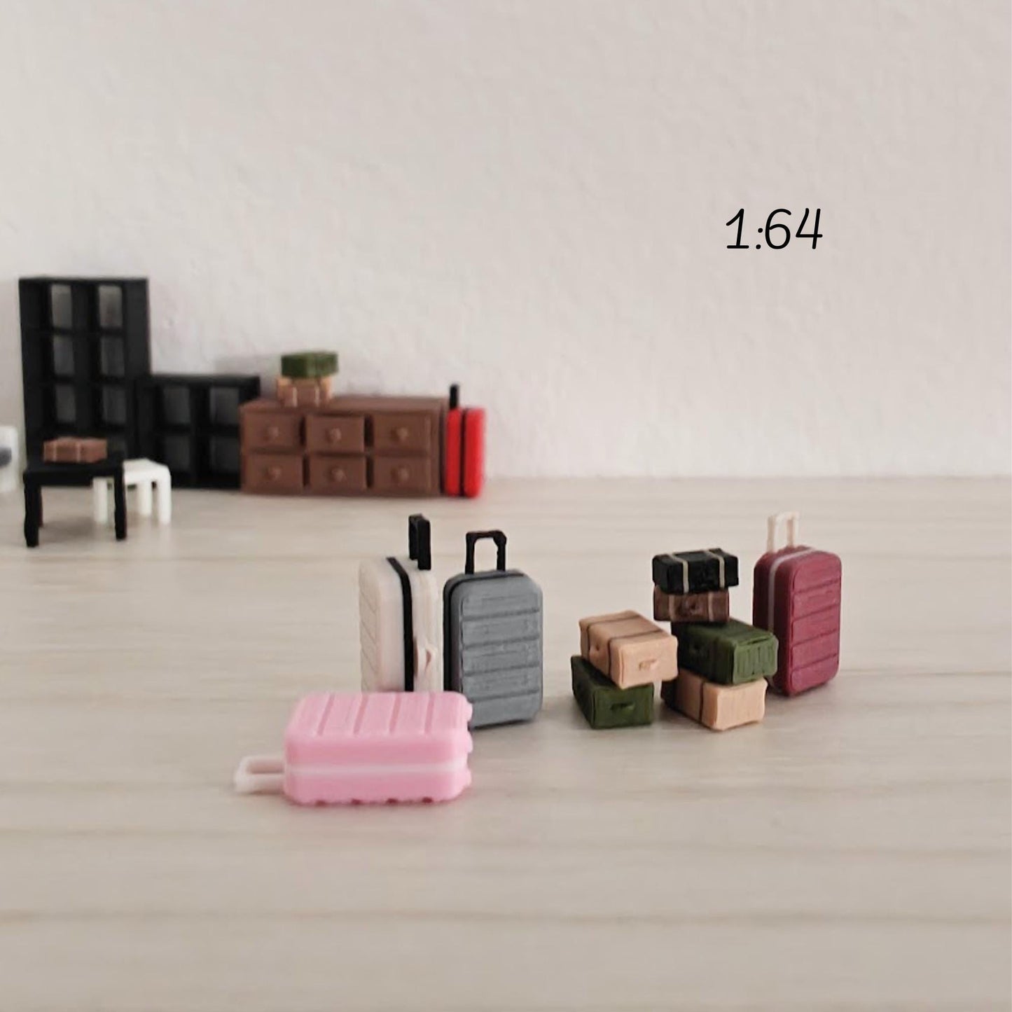 Miniature luggage arranged in a small 1:64 diorama scene with furniture such as tables and cabinets, placed on a light background.