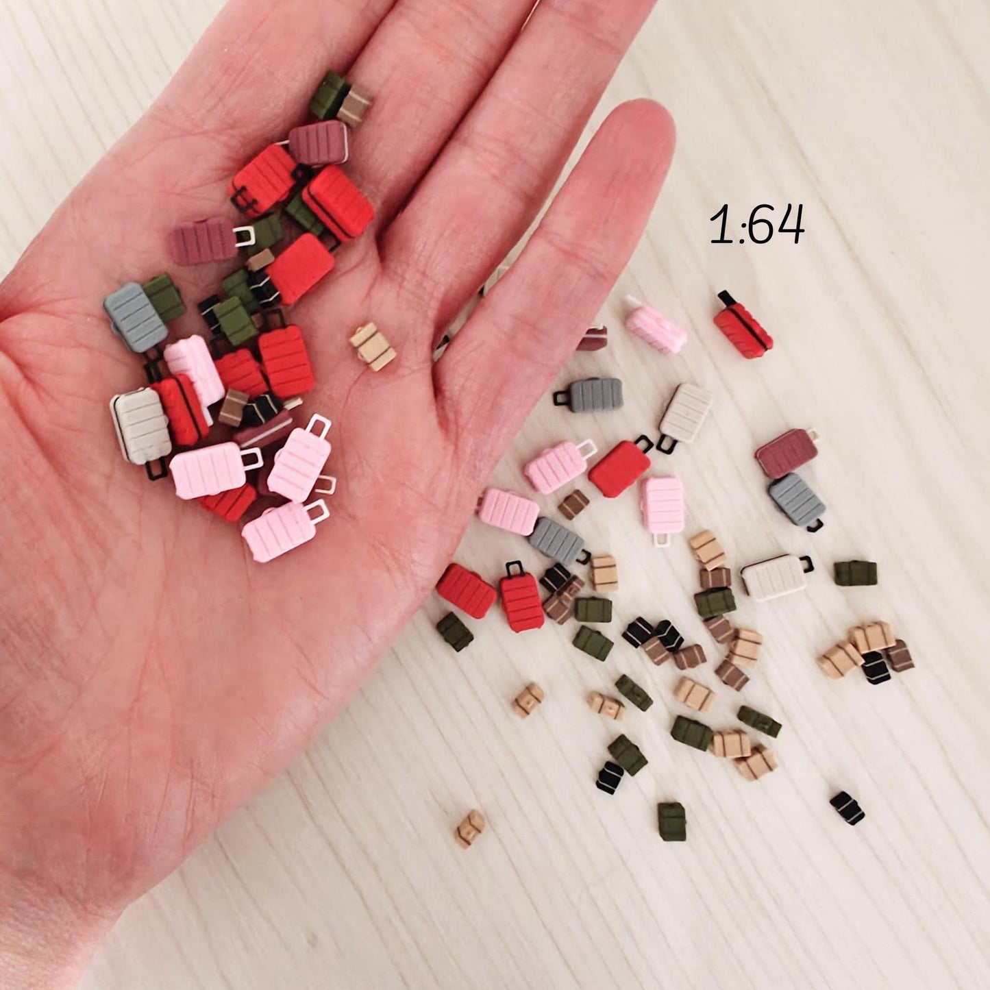 Miniature 3D-printed suitcases in scale 1:64, held in a person’s hand for size reference. Includes various colors such as red, pink, green, and brown.