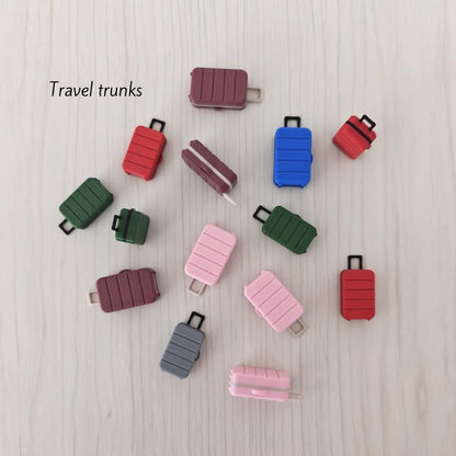 Close-up of colorful 3D-printed miniature luggage, labeled “Travel trunks.” The suitcases have a ridged modern design and include pink, red, green, and blue variants.