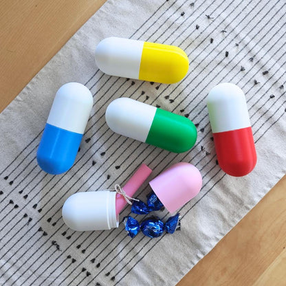 Colorful 3D printed pill capsule boxes in blue, green, yellow, red and pink, displayed open and closed with small wrapped candies inside.