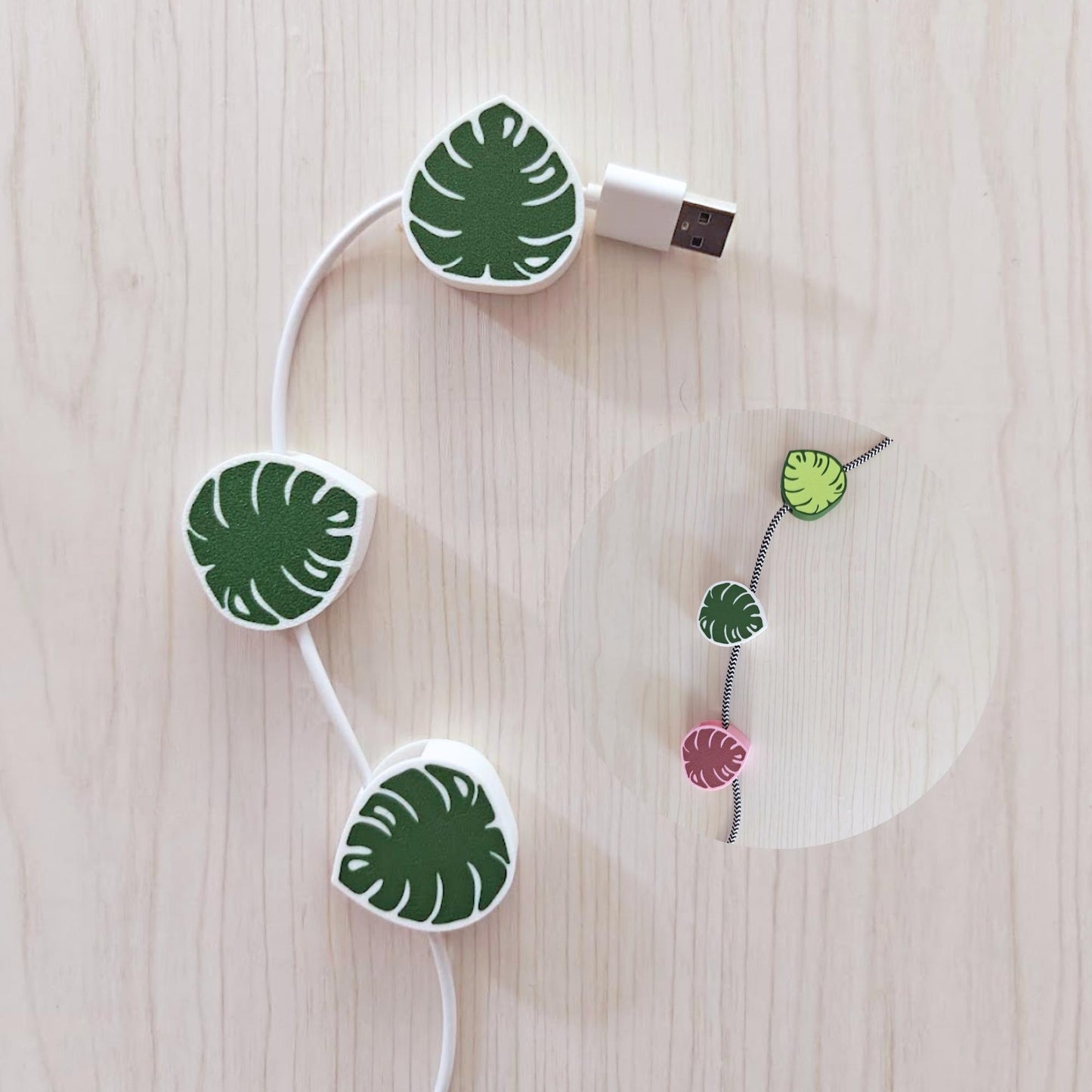 Monstera leaf cable clips holding white cords on a light wood background