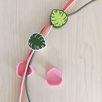 A selection of cable tidies and cord clips. The image features three leaf-shaped cord clips in green and white, and two pink cable organisers.