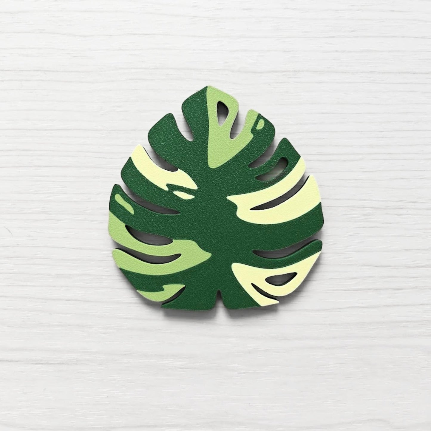 Front view of a Monstera leaf key cover handle for IKEA FABRIKÖR in  leaf green, matcha green, and yellow on a light wood background.