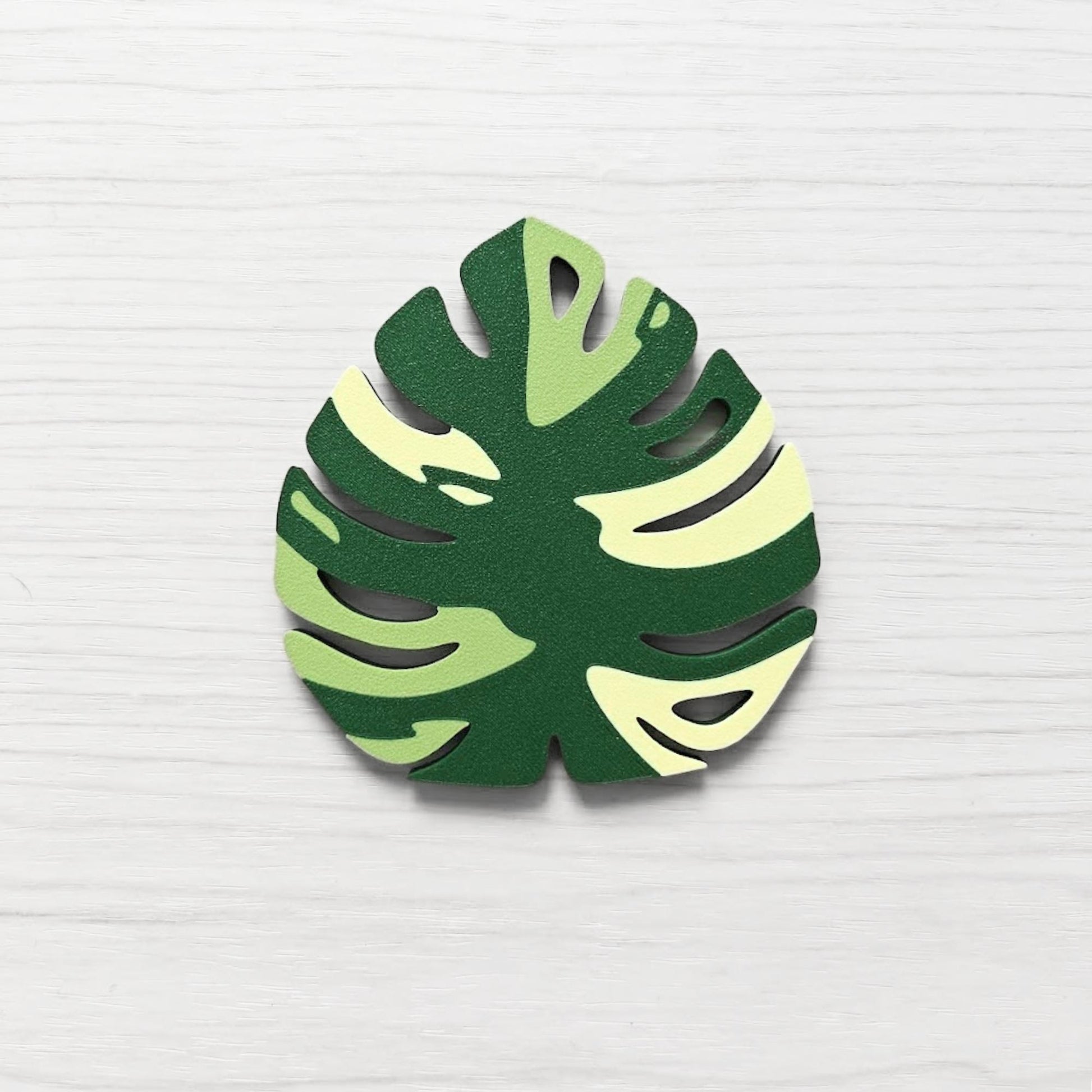 Front view of a Monstera leaf key cover handle for IKEA FABRIKÖR in  leaf green, matcha green, and yellow on a light wood background.