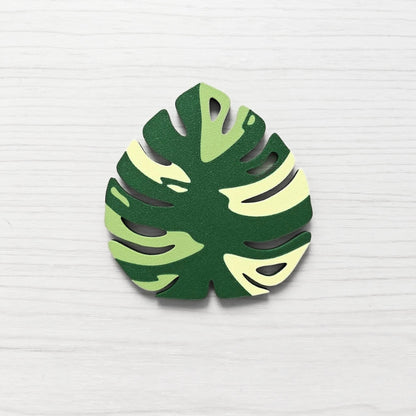 Front view of a Monstera leaf key cover handle for IKEA FABRIKÖR in  leaf green, matcha green, and yellow on a light wood background.