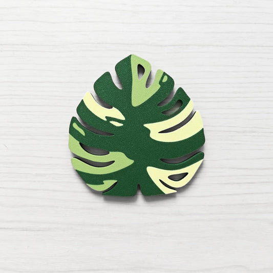 Front view of a Monstera leaf key cover handle for IKEA FABRIKÖR in  leaf green, matcha green, and yellow on a light wood background.