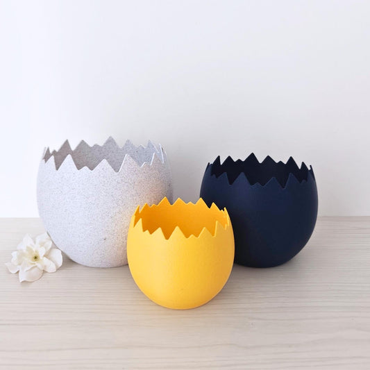 Set of cracked eggshell planters in white, yellow, and dark blue on a neutral surface