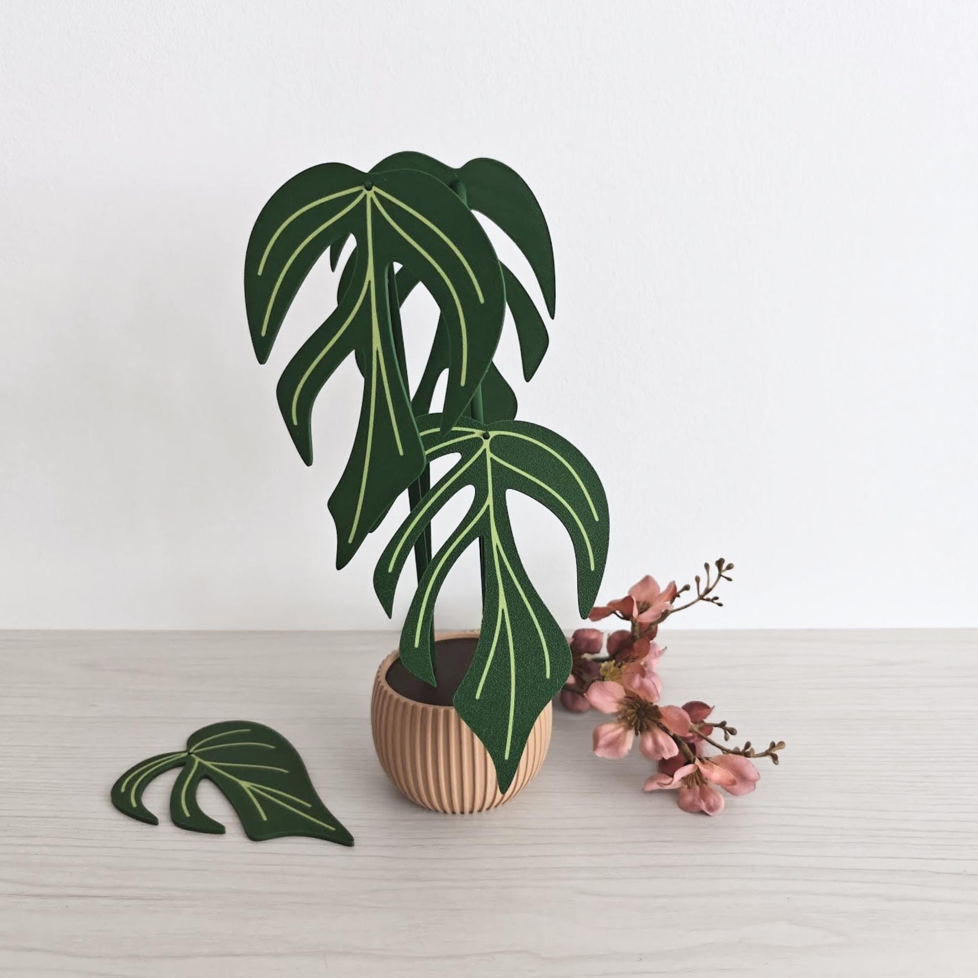 Monstera Burle Marx Flame coaster set displayed stacked upright in a small brown pot-shaped holder, with one coaster placed in front and pink flowers beside it.