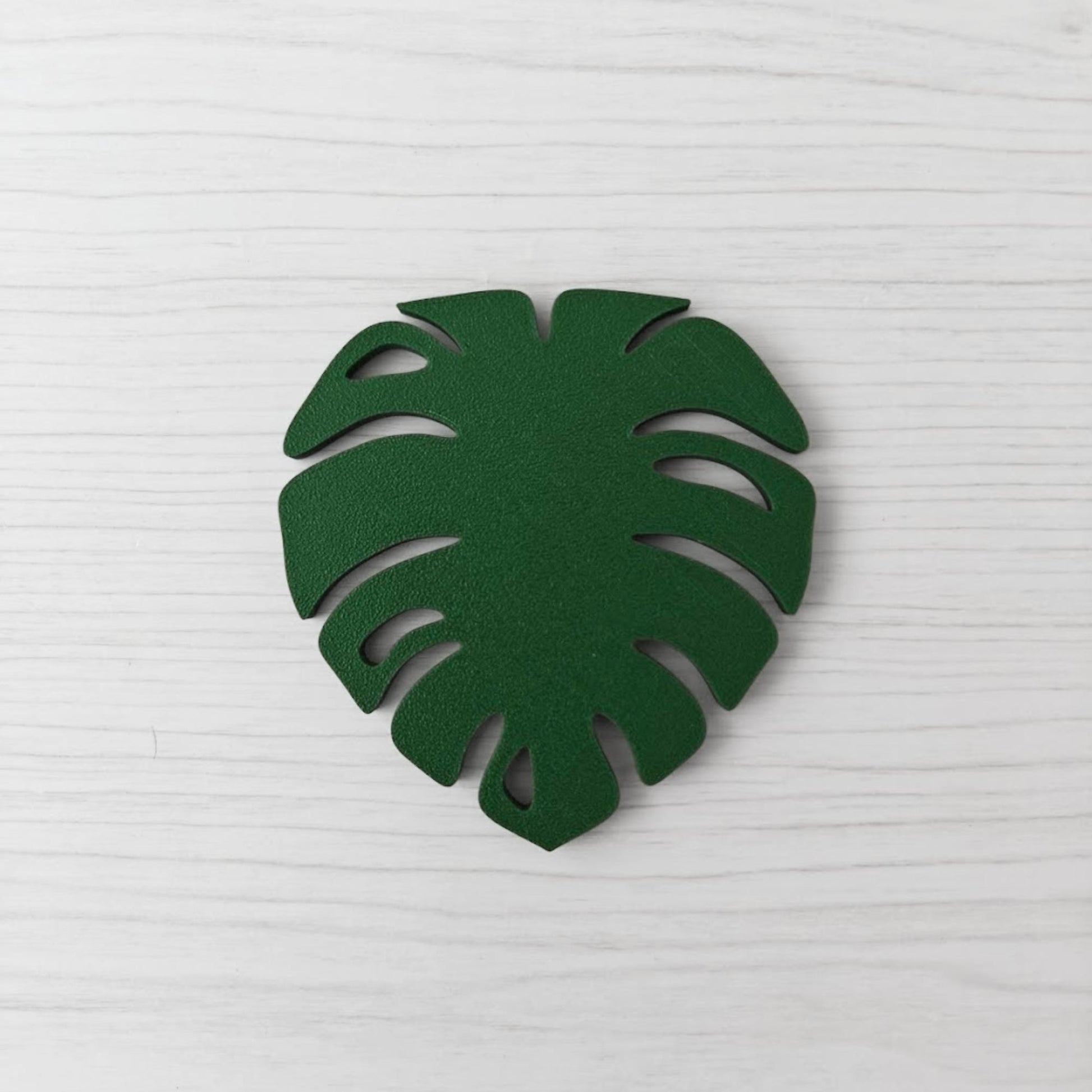 Front view of the solid leaf green Monstera leaf key cover handle on a light wood background.