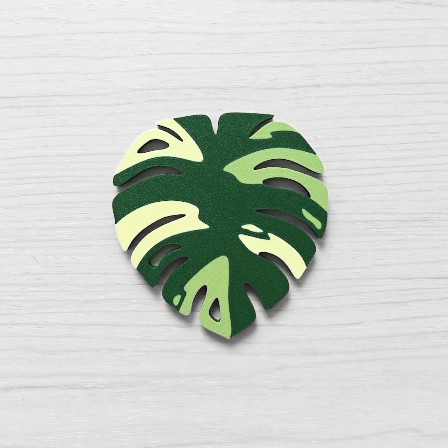 Front view of a Monstera leaf key cover handle for IKEA FABRIKÖR in  leaf green, matcha green, and yellow on a light wood background.