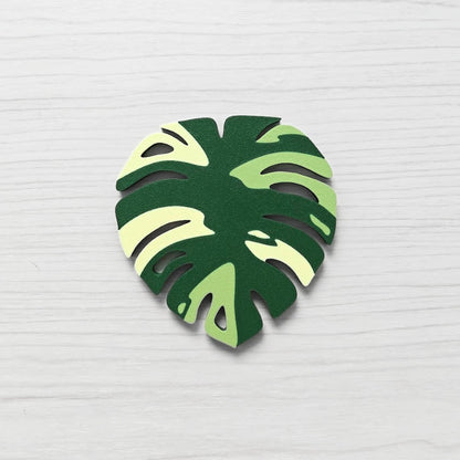 Front view of a Monstera leaf key cover handle for IKEA FABRIKÖR in  leaf green, matcha green, and yellow on a light wood background.