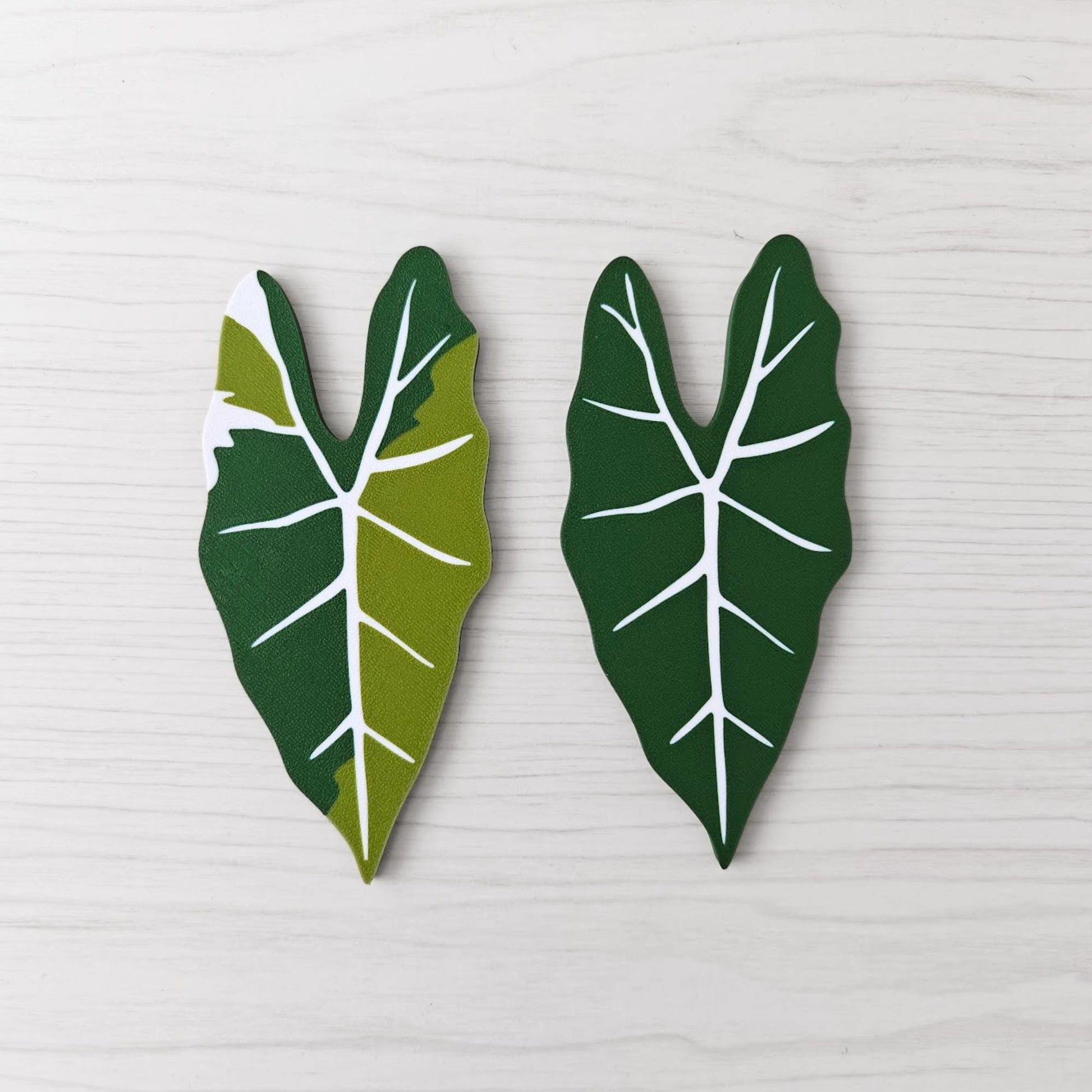 Front view of two Alocasia Frydek key cover handles for IKEA FABRIKÖR, shown in solid green and green with white variegation on a light wood background.