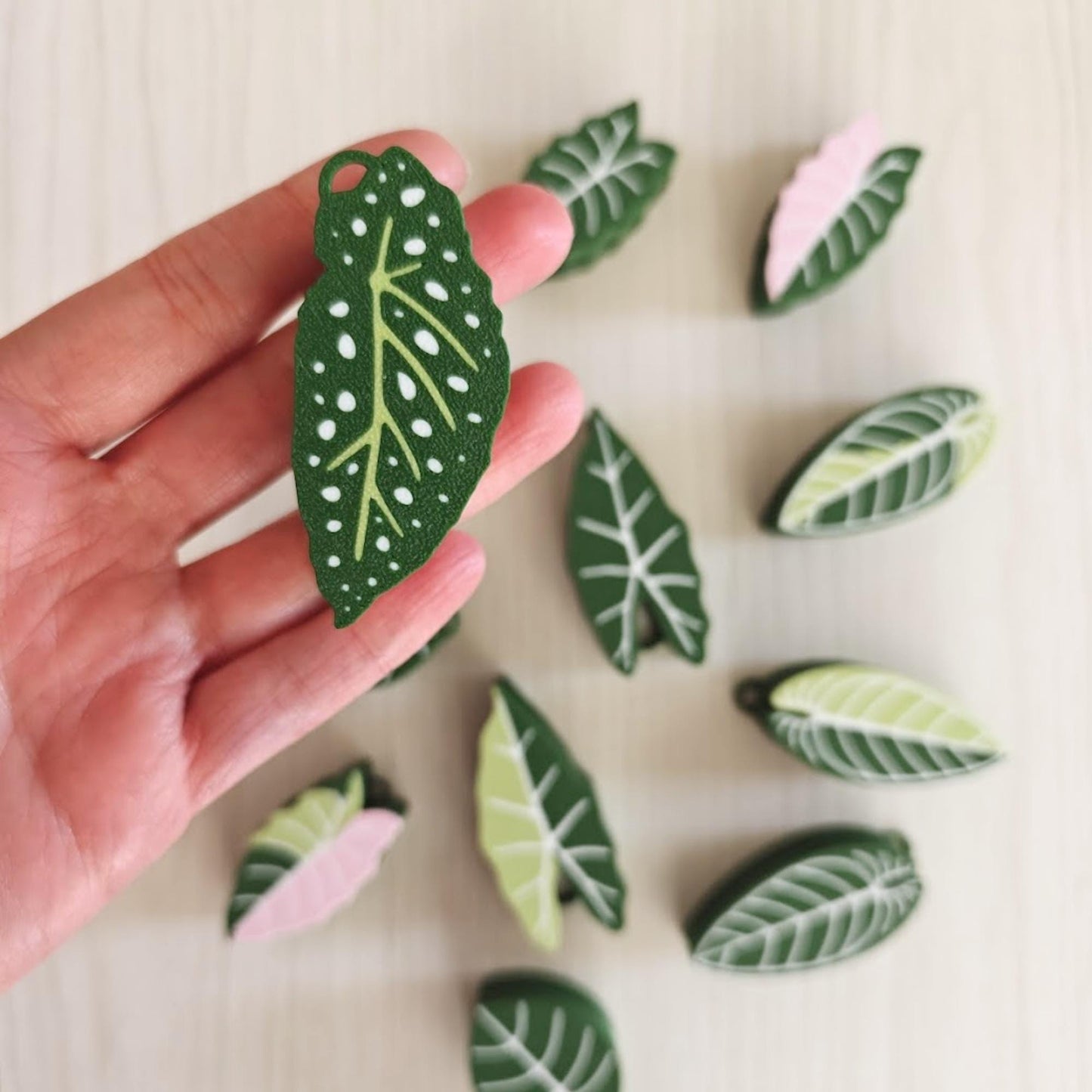 Hand holding green leaf clicker fidget with multiple designs in background