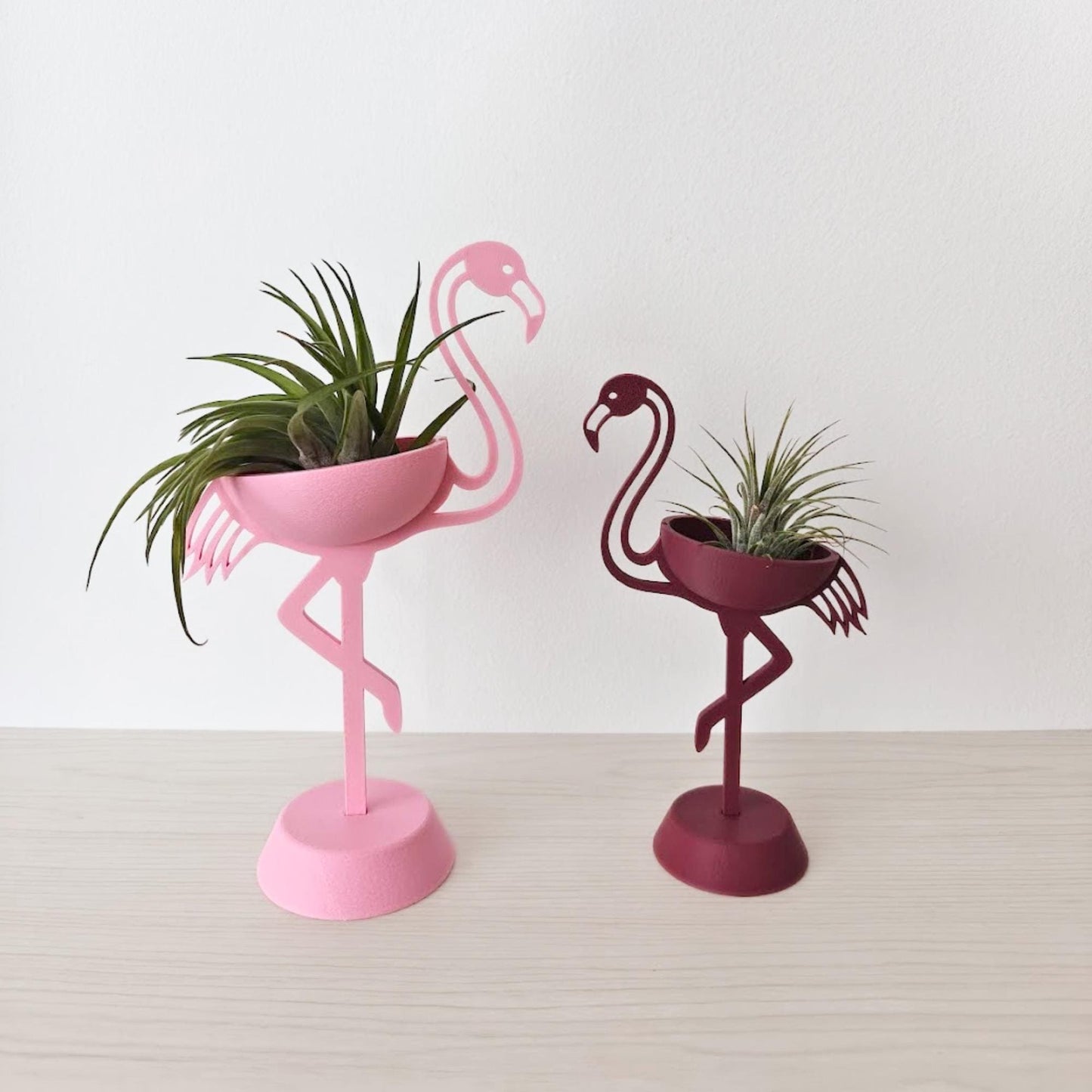 Pink and burgundy flamingo air plant holders with Tillandsia plants on a wooden table