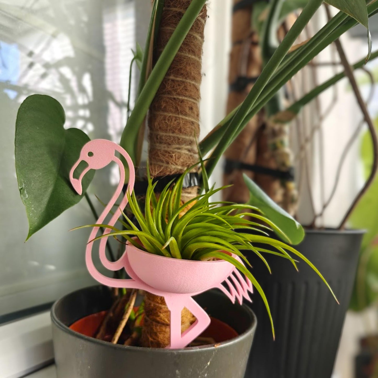 Pink flamingo plant holder placed inside pot among houseplants