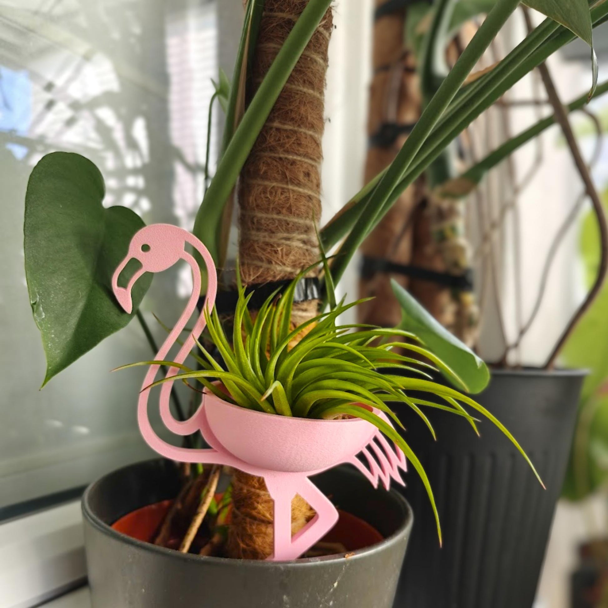 Pink flamingo plant holder placed inside pot among houseplants