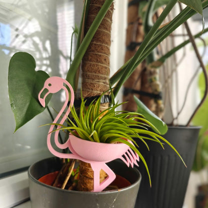 Pink flamingo plant holder placed inside pot among houseplants