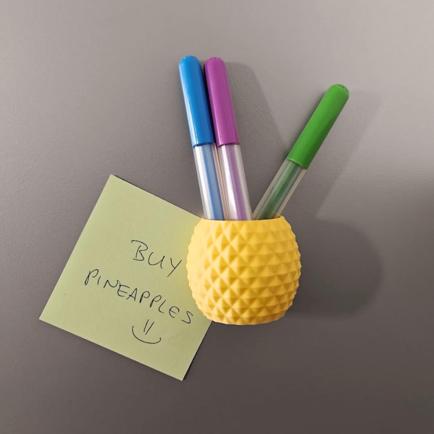 Pineapple magnet used as pen holder with sticky notes on a metal surface