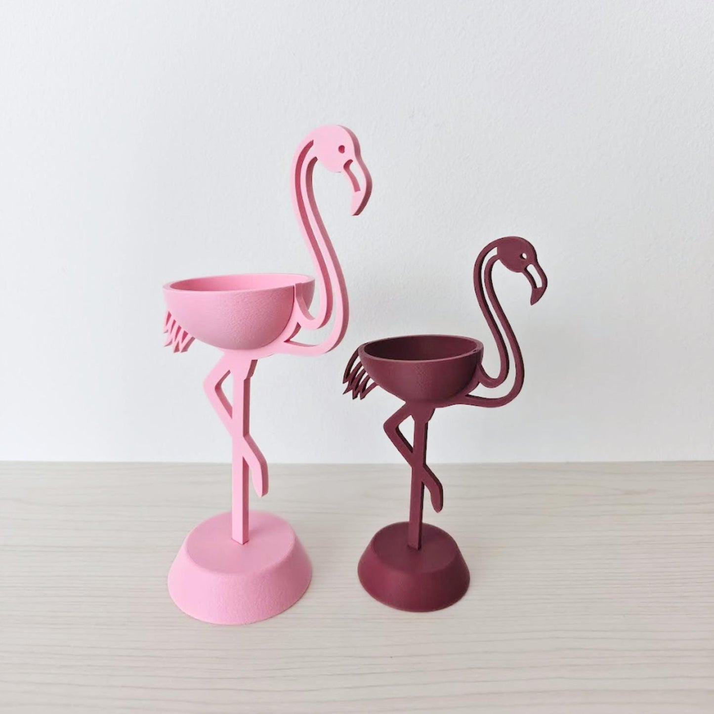 Pink and burgundy flamingo plant holders without plants on neutral background