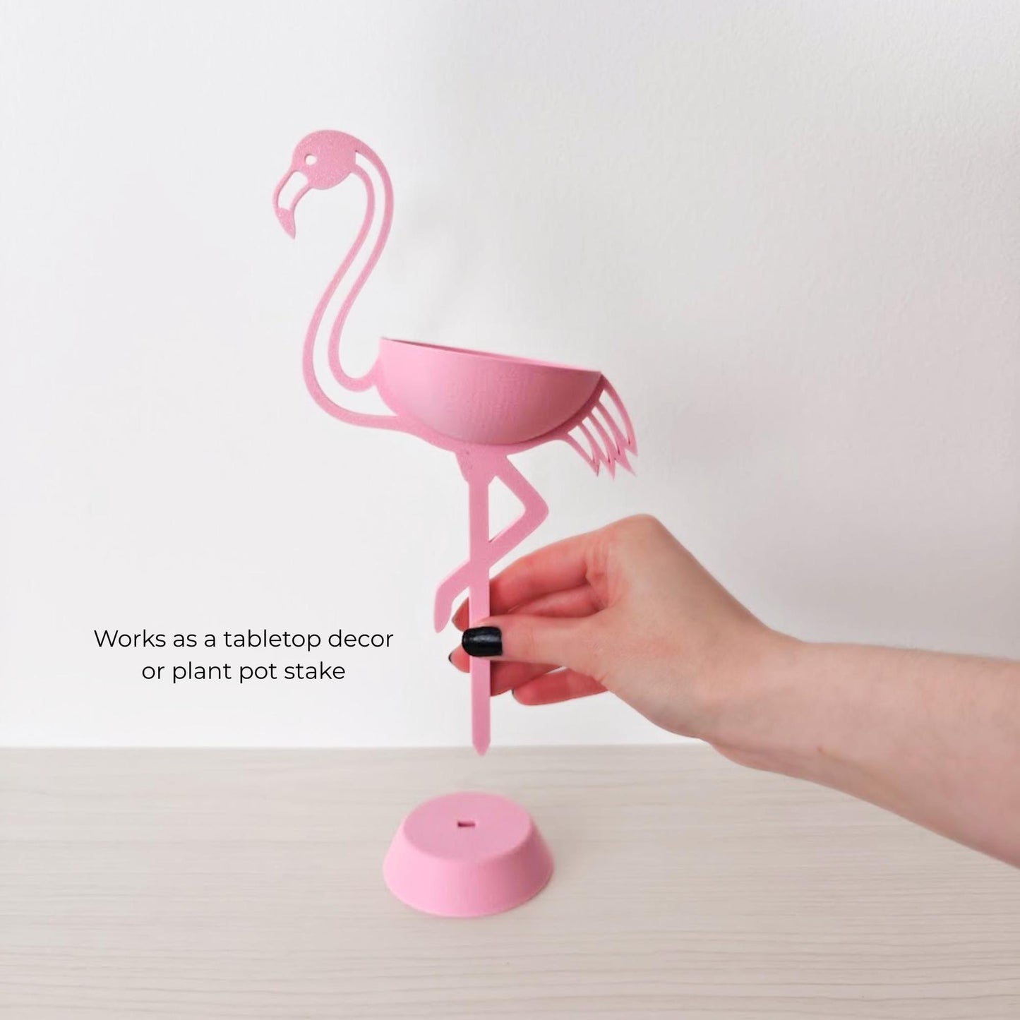 Hand holding flamingo plant holder showing removable base and stake use