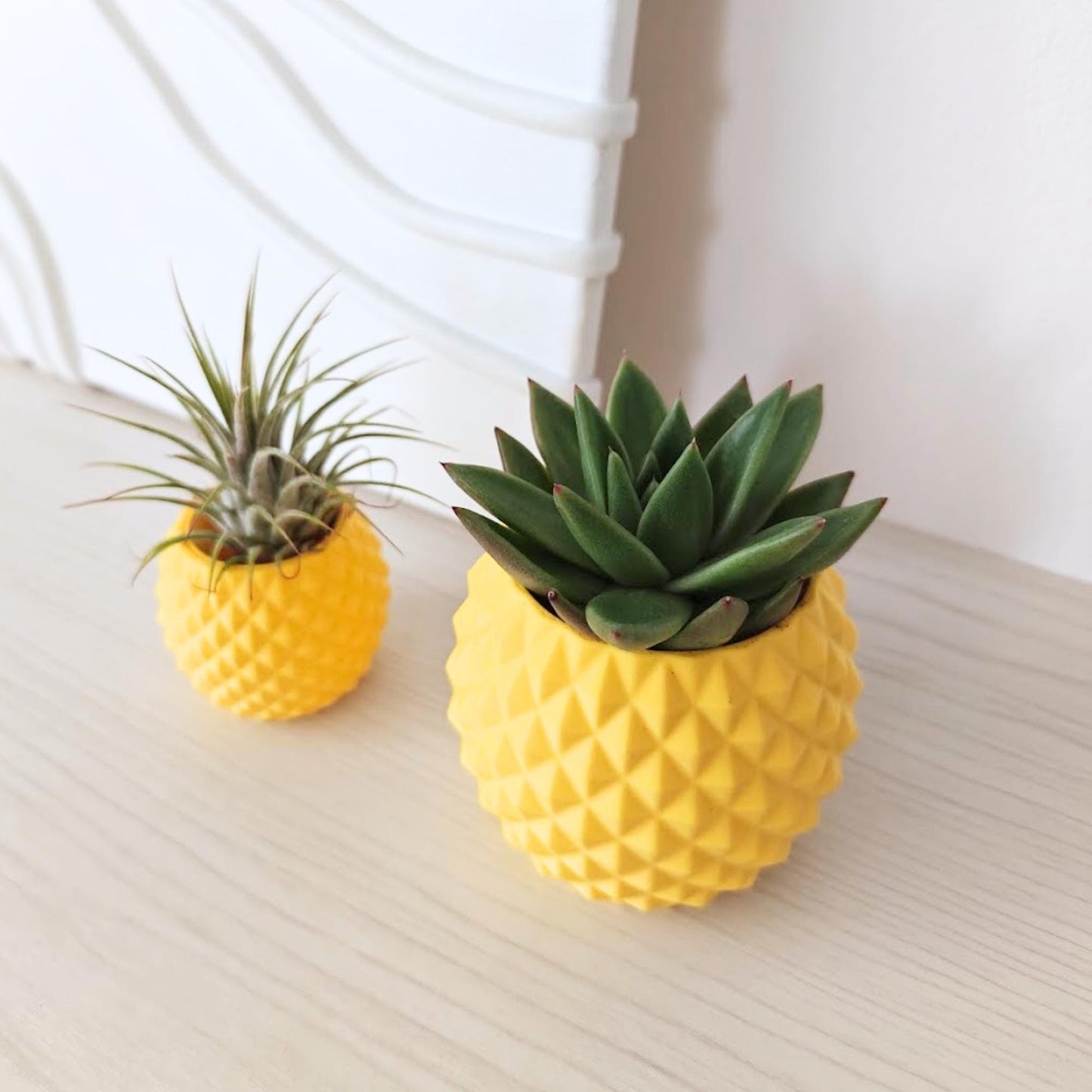 Yellow pineapple planters with air plant and succulent on a wooden surface, minimalist decor background