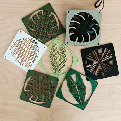 Monstera fan cover 120mm collection, plant-themed PC fan grills in multiple leaf designs and colors on wooden background
