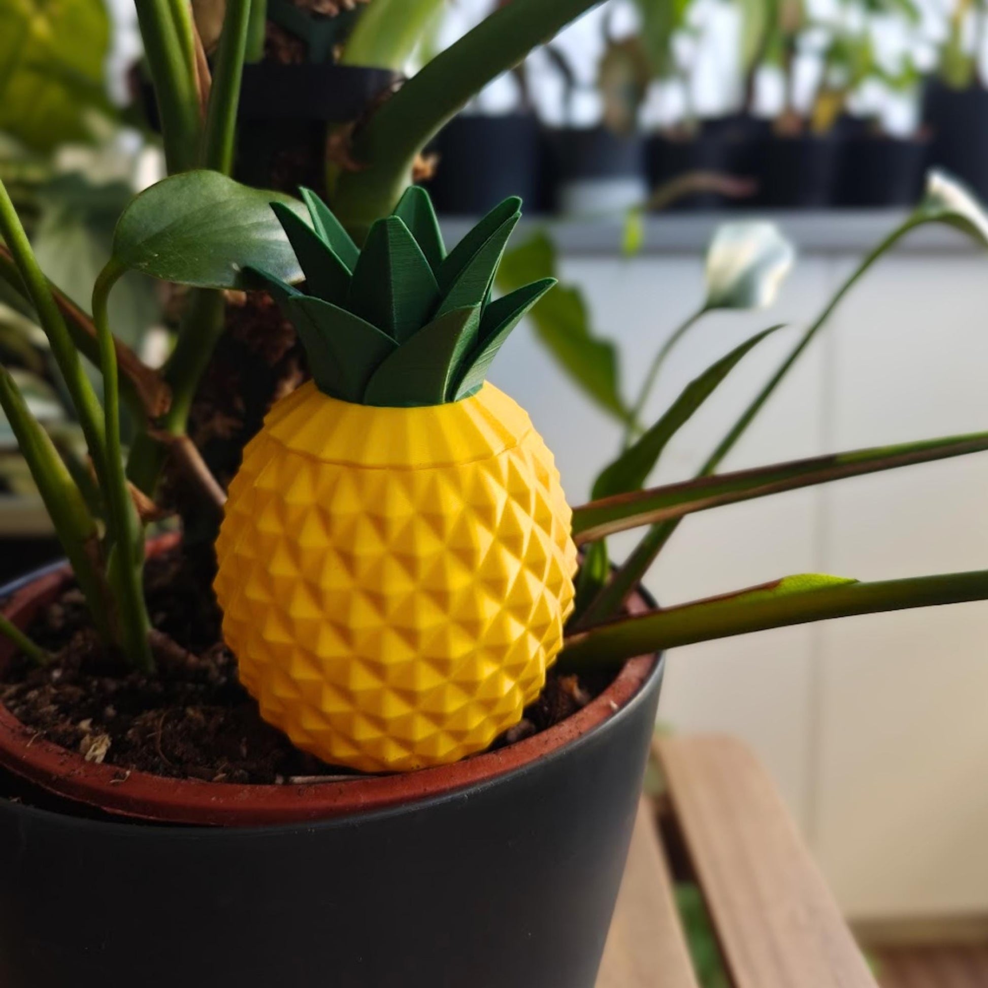 Pineapple-shaped watering spike placed in a potted houseplant with removable leafy lid attached.
