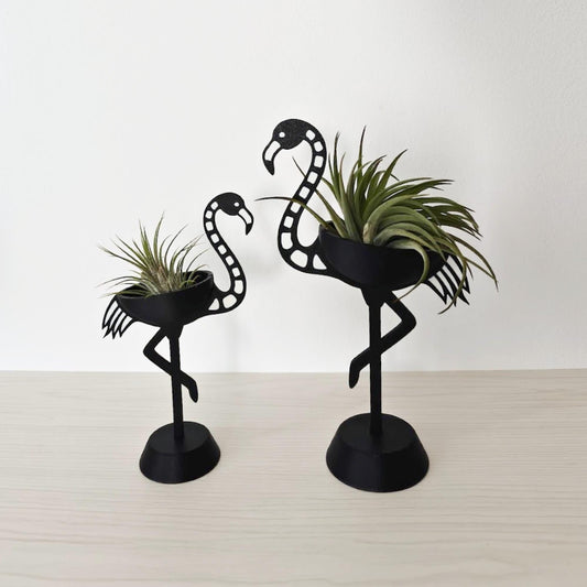 Two skeleton flamingo air plant holders in black, small and large size, placed on a light surface